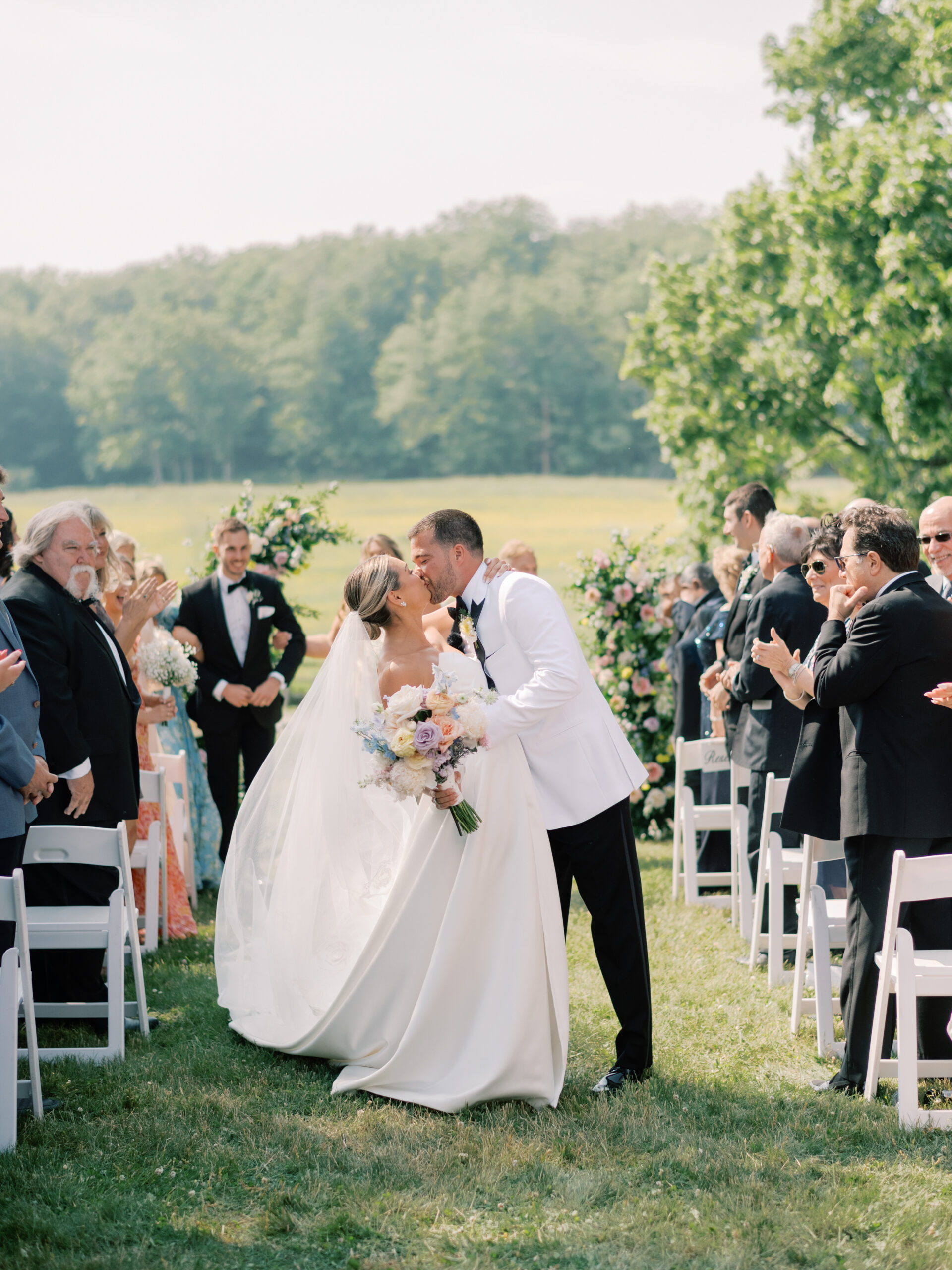 BRIDE AND GROOM KISSING IN Front of guests in photo from wedding at know farms in east auroroa